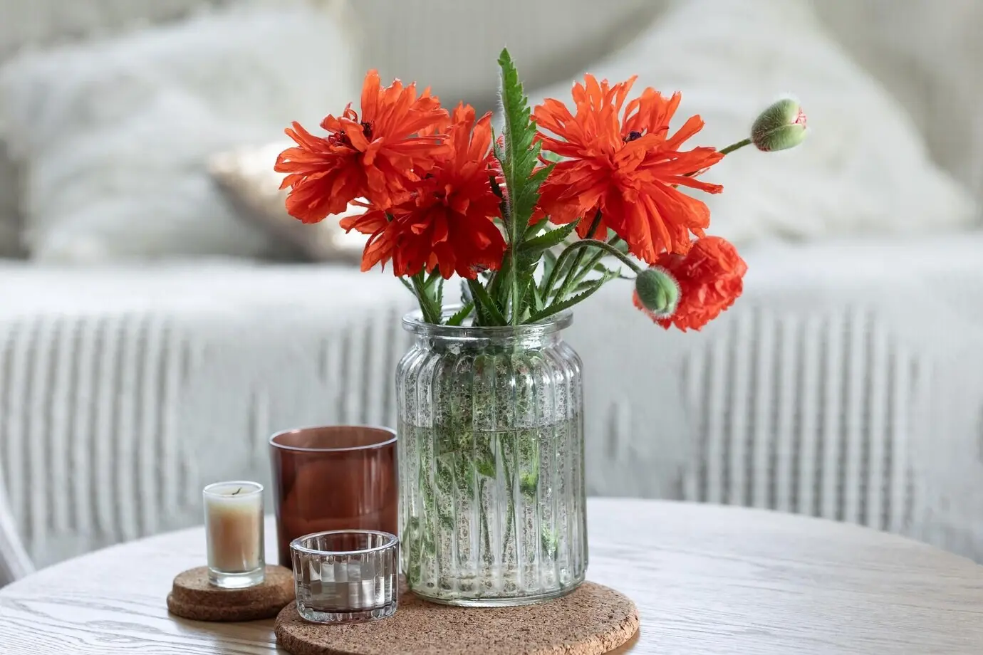 Ein minimalistisches Arrangement aus roten Mohnblumen in einer Vase und Kerzen zu Hause.