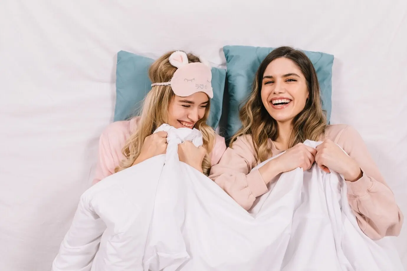 Ansicht von oben auf lachende Frauen im Bett.