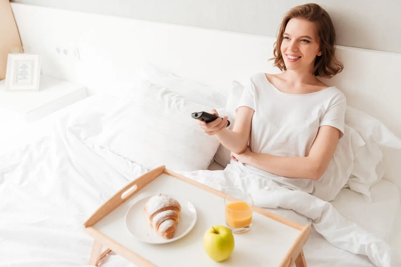 Fröhliche junge Frau schaut fern und hält eine Fernbedienung.